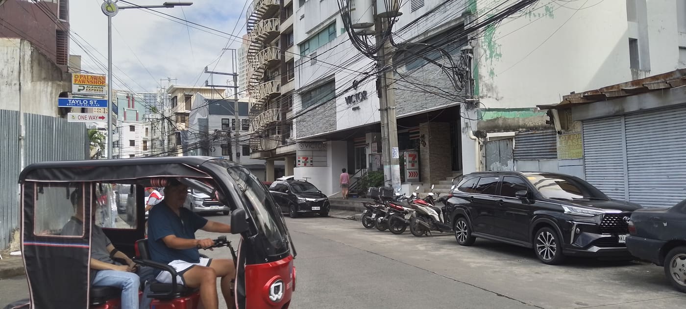 マニラの通り(Taylo St.付近)を走るトライシクル(屋根付き三輪タクシー)。バイクや車、コンビニや質屋の看板が並ぶ下町の風景